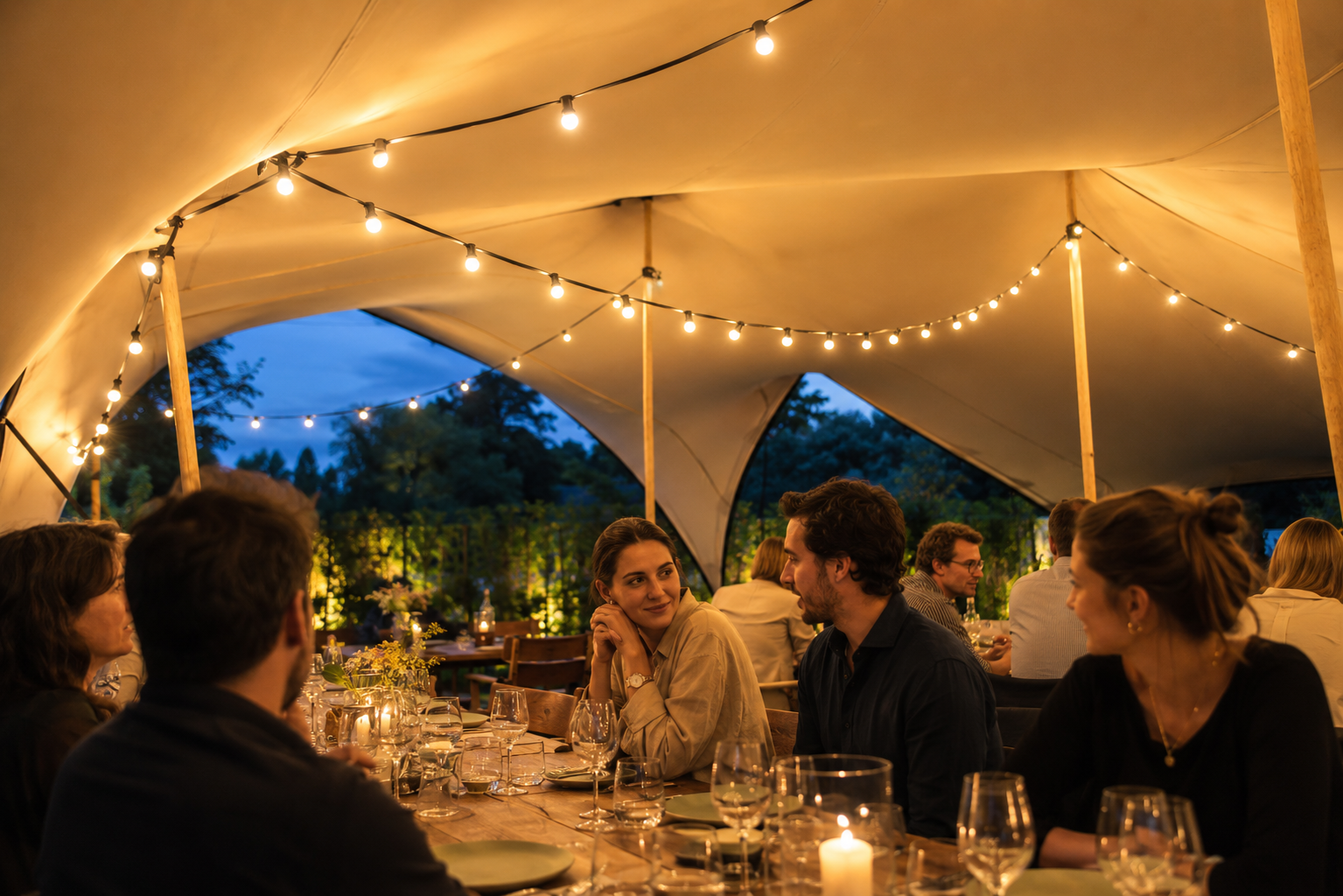 Dîner sous une tente stretch éclairée par des guirlandes à la nuit tombée